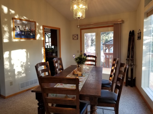 A dining room with a long wooden table, six chairs, a chandelier, and a painting on the wall.
