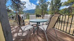 A wooden deck with a round table and chairs, surrounded by a metal fence, overlooking a mountainous landscape. - Eagle Cliff Cottage Sleeps 6 ((20-NCD0244) (Estes Park)