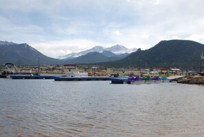 Ein Yachthafen mit angestaubten Booten, eine kleine Pier mit bunten Stühlen und Berge im Hintergrund.