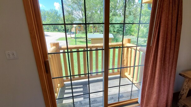 Blick aus einem Zimmer mit einer Schiebeglastür zu einer Terrasse mit Holzgeländer.