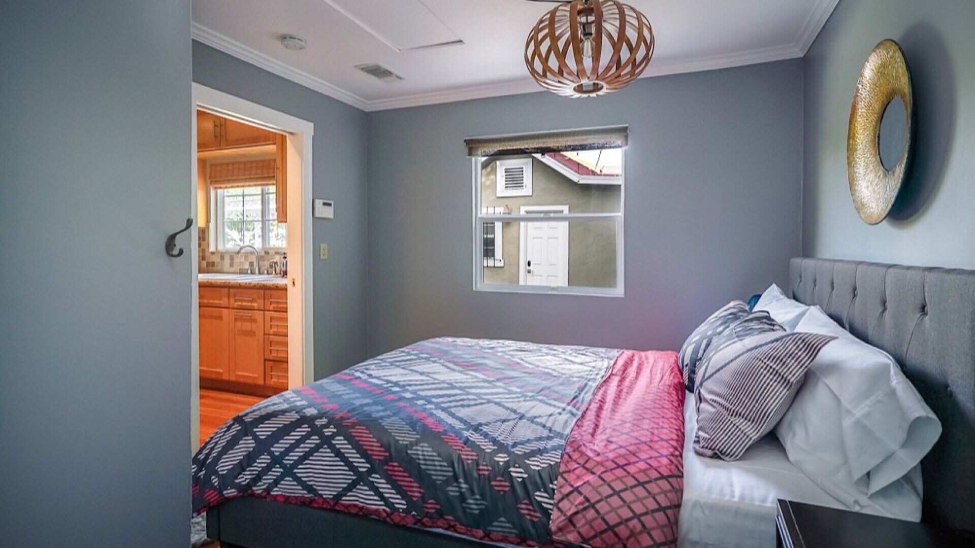 A bedroom with a bed, a window, a door, and a hanging light fixture.