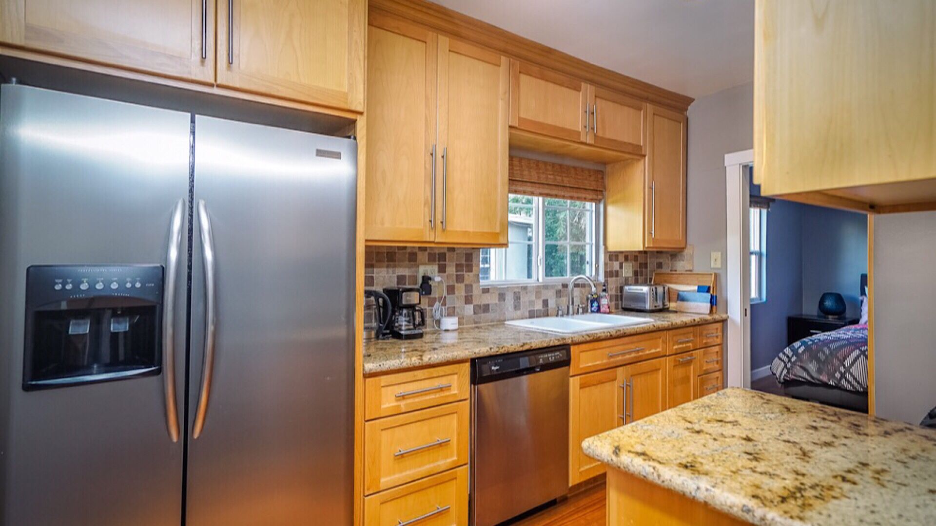 A modern kitchen with wooden cabinets, stainless steel appliances, a water dispenser, and a granite countertop.