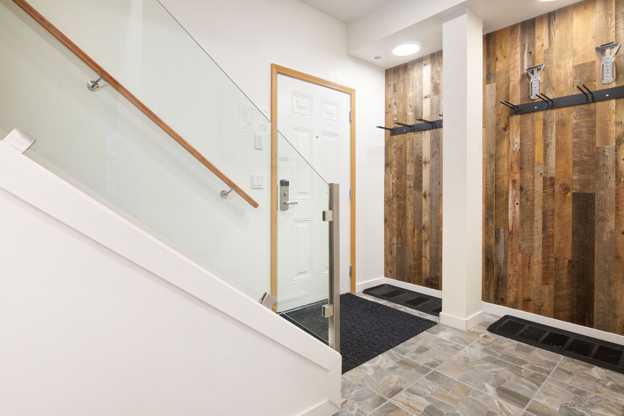 A modern interior with a glass staircase, a wooden accent wall, and a black carpeted entrance.
