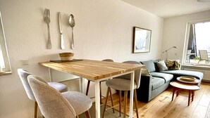 En moderne stue med et træspisebord, to grå stole, en grå sofa og et lille rundt bord med en skål.