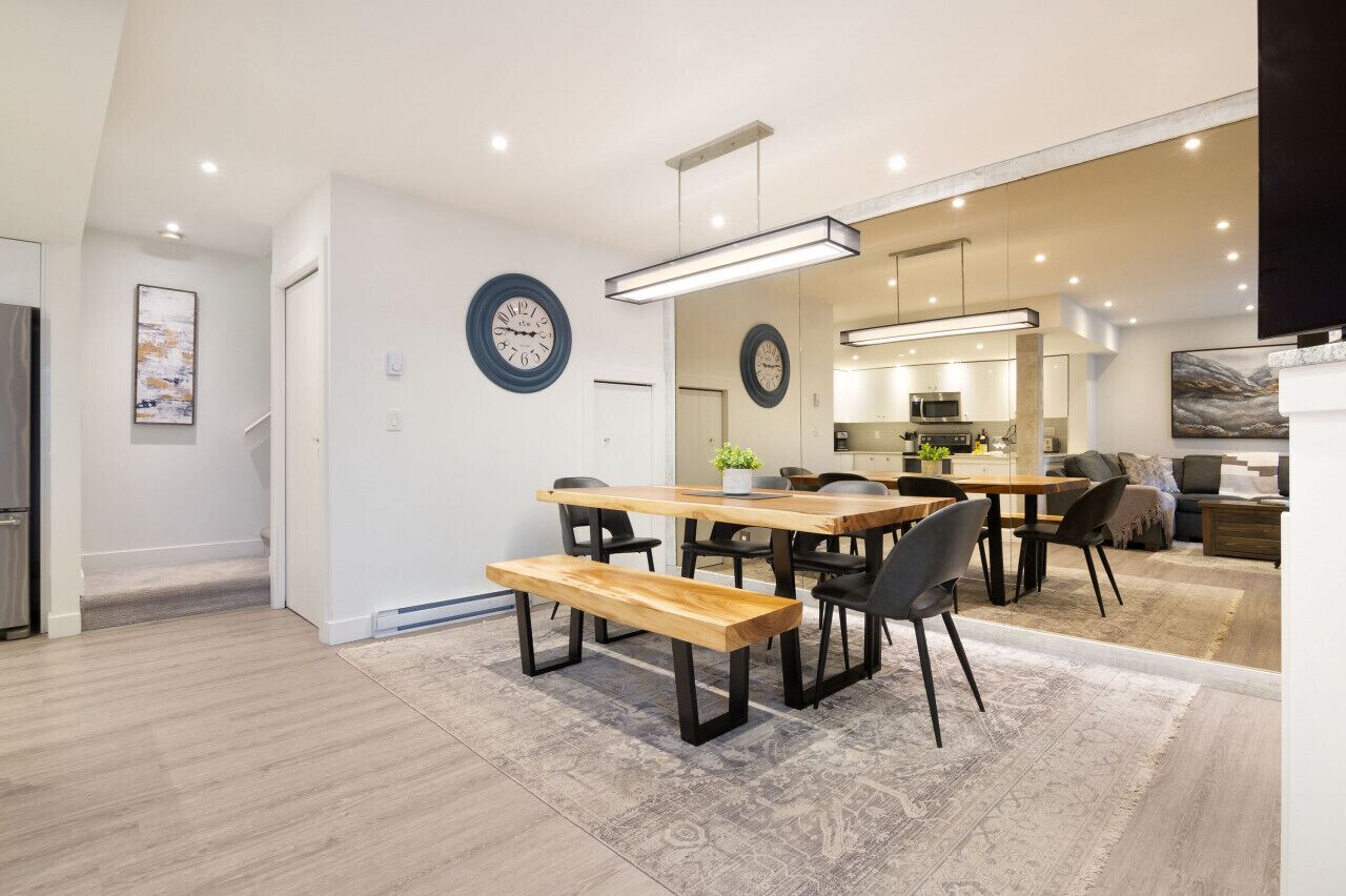 A modern kitchen with a central island, a dining area with a wooden table and benches, and a living area with a sofa and a coffee table.