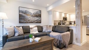 A modern living room with a sectional sofa, a coffee table, and a large abstract painting on the wall. - Luxury 3Br TH- Private Hot Tub/AC/Pool/Bike Storage (Whistler)