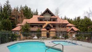 A large building with a distinctive triangular roof and a swimming pool area with two pools and a deck. - Luxury 3Br TH- Private Hot Tub/AC/Pool/Bike Storage (Whistler)