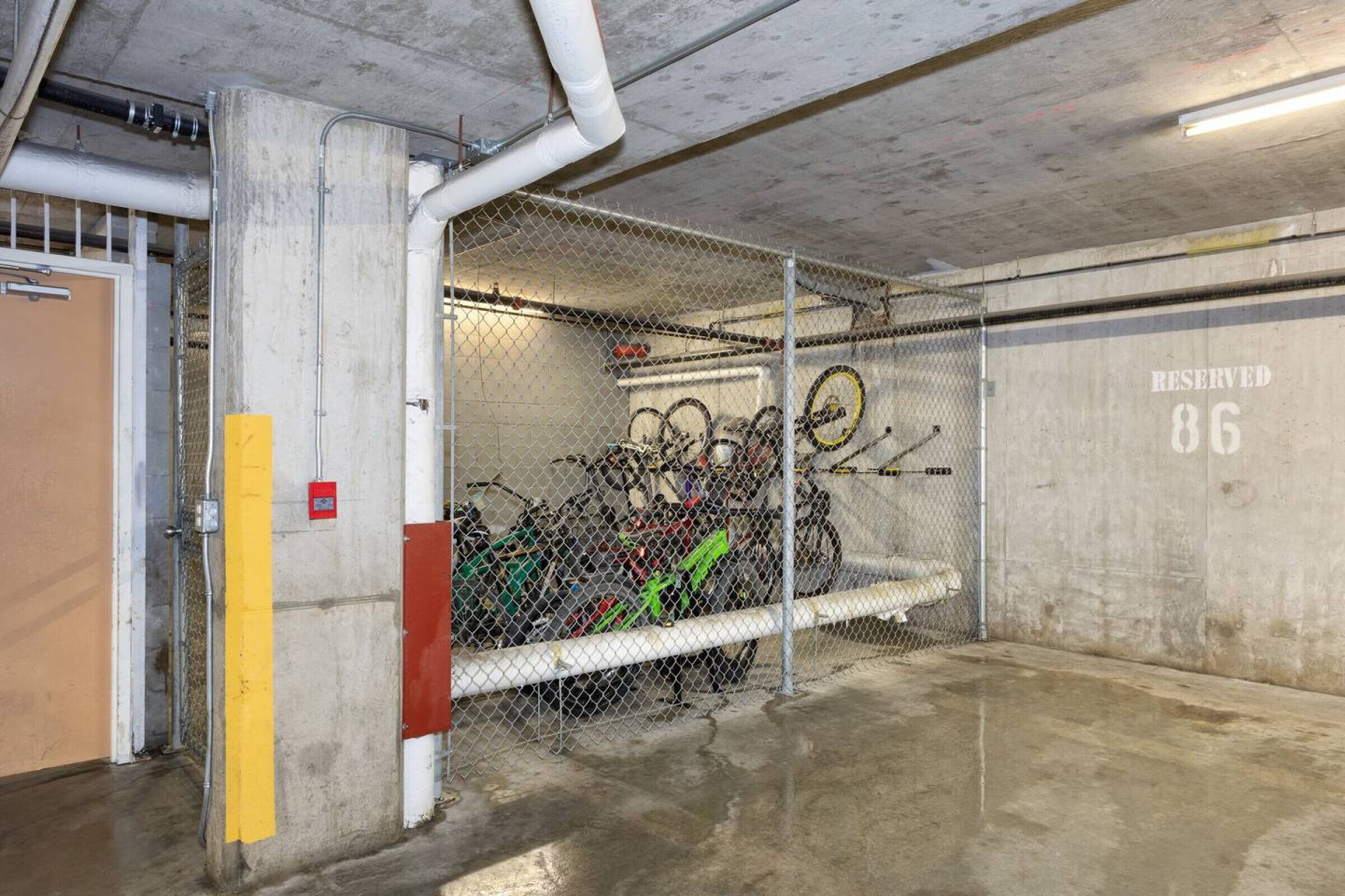 Un estacionamiento con cerca de malla metálica, bicicletas y un letrero de área reservada.