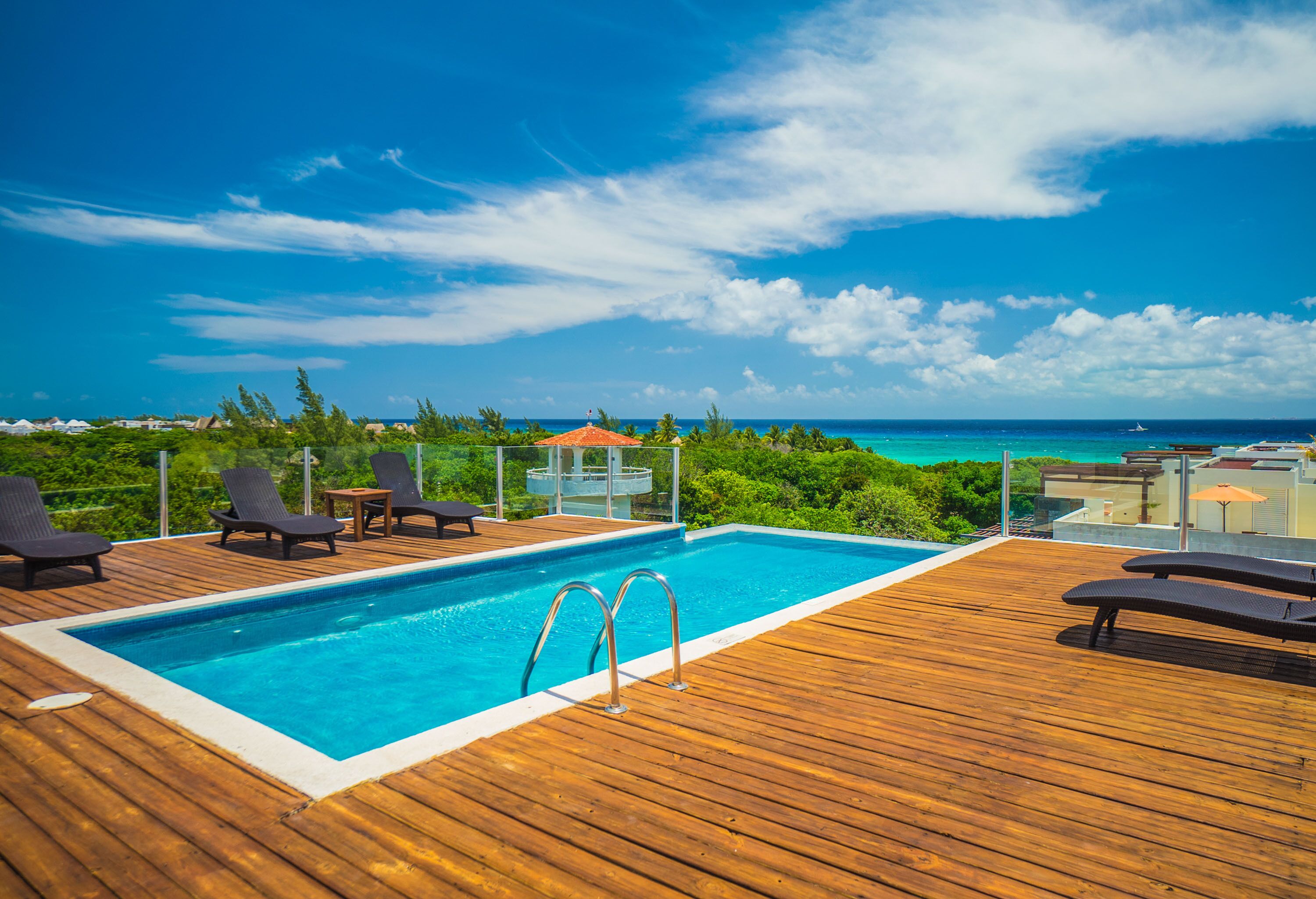 A wooden deck with a pool, lounge chairs, and a view of the ocean.