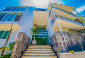 A modern building with a staircase leading to a glass entrance, surrounded by palm trees.