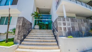 Un edificio moderno con una scala che conduce a un ingresso in vetro, circondato da mura in pietra e palme.