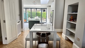 A modern kitchen with a glass dining table, white cabinetry, and a view to the outdoors. - Beautiful 4 bedroom Victorian family house on quiet road (London)