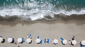 Une vue aérienne d’une plage où l’on aperçoit des rangées de parasols et de chaises longues, dont certaines sont occupées par des personnes.