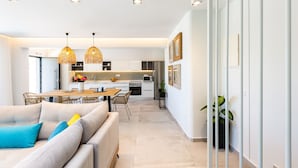 Une cuisine moderne avec des meubles blancs, un coin repas doté de chaises en osier et un éclairage suspendu.