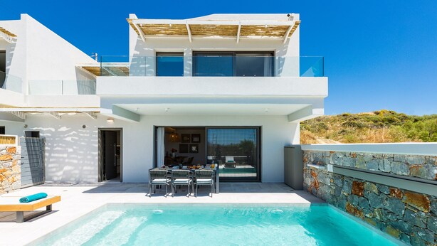 Une maison moderne à deux étages, dotée d’une piscine, d’un espace de détente extérieur et de murs en pierre.