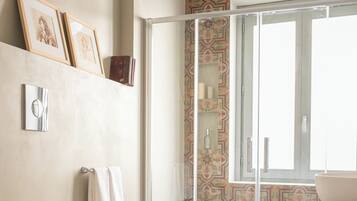 Un baño con dos lavamanos grandes de color blanco, una cabina de ducha con paredes de vidrio y baldosas de suelo estampadas.