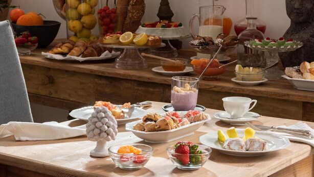 A buffet table with various food items, including fruits, pastries, and a glass of a purple beverage.