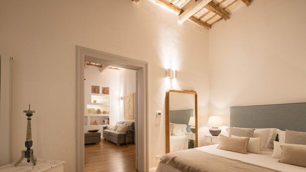 A bedroom with a large bed, a bedside table with a lamp, a mirror, and a wooden ceiling. - Dimora Botteghelle (Trapani)