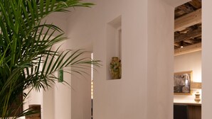 A hallway with a potted plant, a rustic ceiling, and a dining area with a chair and table. - Dimora Botteghelle (Trapani)