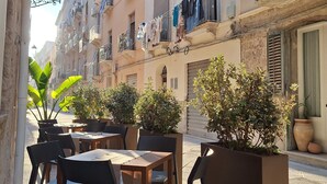An outdoor café with tables and chairs, surrounded by potted plants and buildings with balconies. - Dimora Botteghelle (Trapani)
