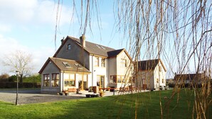 Une maison à deux étages avec une grande pelouse devant, un patio et une cheminée bien visible.