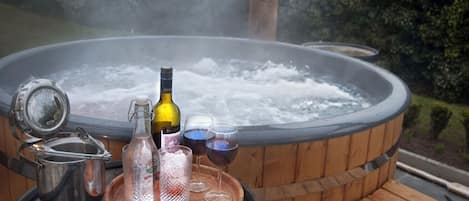 A hot tub with a wooden deck, a metal pot, a bottle, and two glasses filled with water.