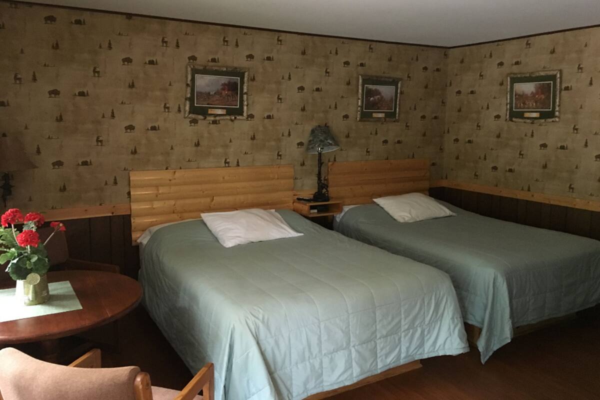 Habitación de hotel con dos camas individuales, cabecera de madera, una mesita redonda con un florero y una lámpara.