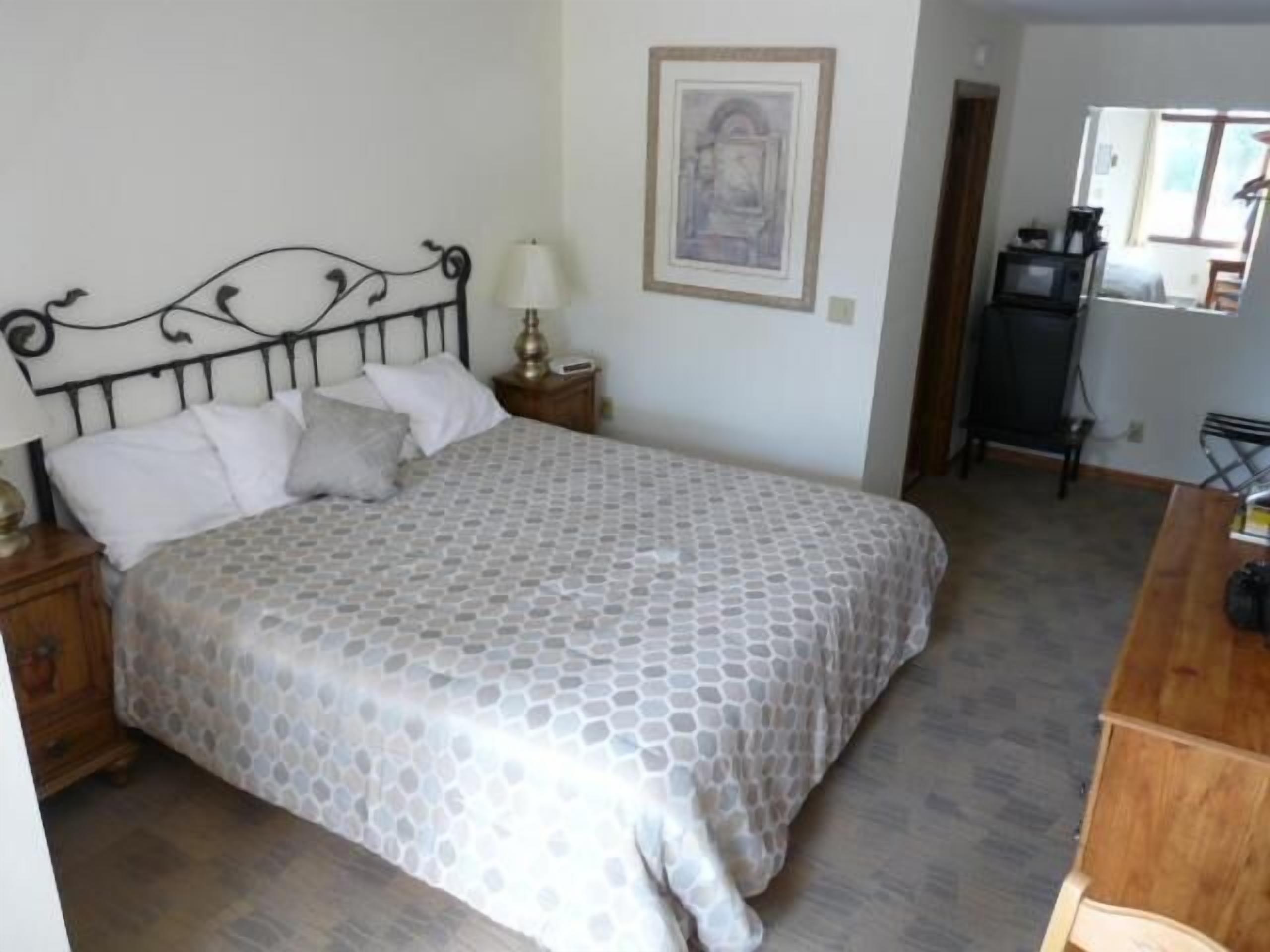 Een slaapkamer met een bed, nachtkastje, lamp en een lijst aan de muur.