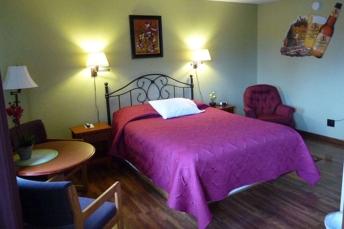Habitación de hotel con cama, dos lámparas de noche, una silla, una mesita y un adorno en la pared.
