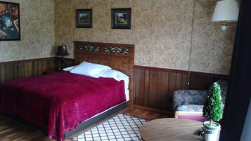Un dormitorio con una cama de madera, una mesita redonda con una planta en maceta, una silla y un cabecero decorativo.