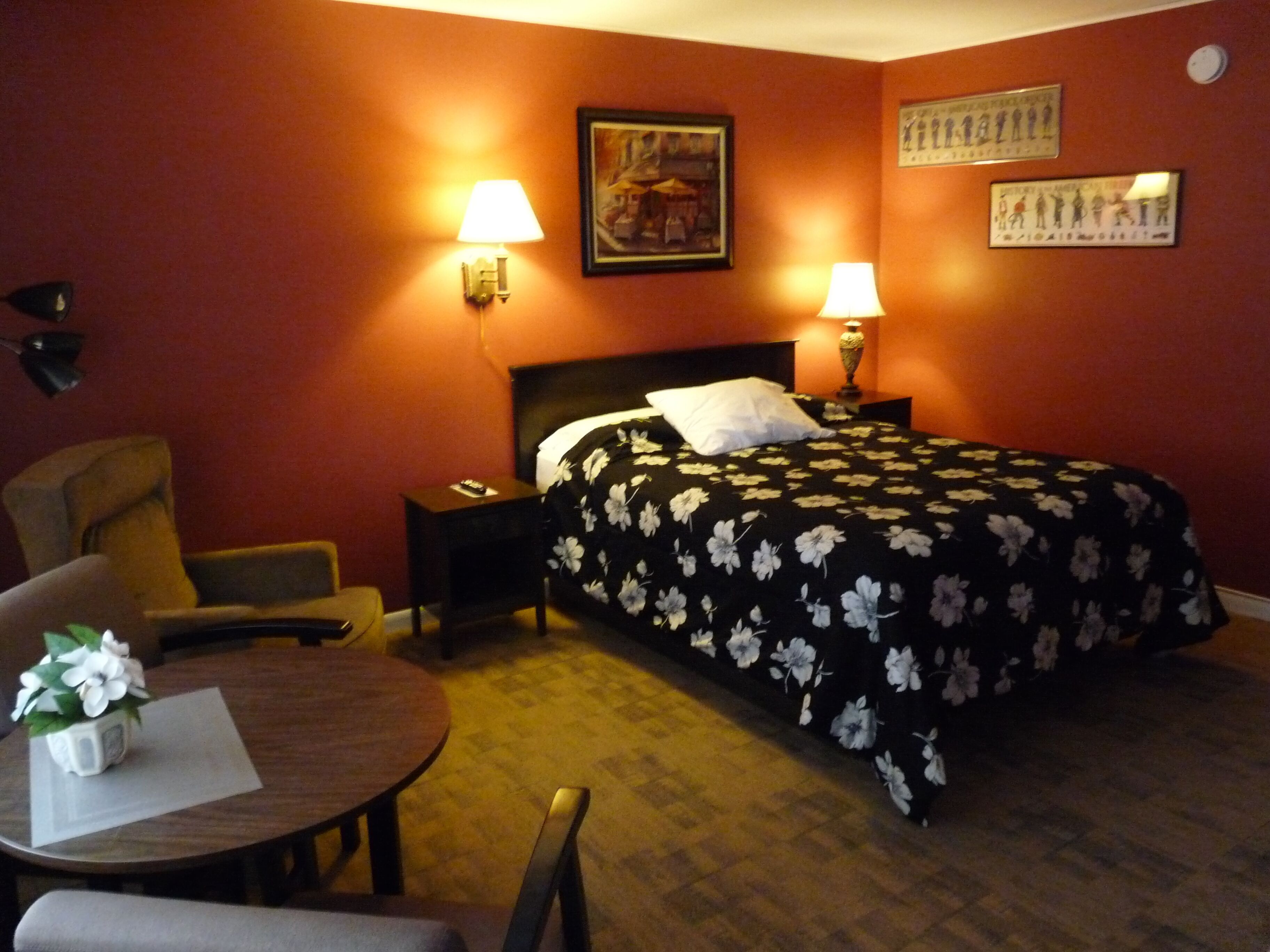 A hotel room with a bed, two bedside lamps, a chair, a small table, and a painting on the wall.