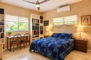 Un dormitorio con una cama, un escritorio, sillas, una estantería y una ventana con persianas.