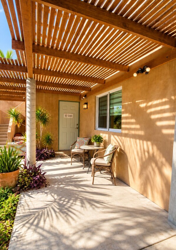 Un patio exterior con una pérgola de madera, una puerta con la etiqueta 'Studio' y una mesa con sillas.