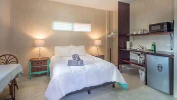 Ein Schlafzimmer mit Bett, Nachttischen, Schreibtisch, Kleiderschrank, Mikrowelle und Kühlschrank.