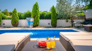 A poolside area with lounge chairs, a glass of water, and two glasses of orange juice on a table. - Villa Delle Rondini with private pool (Bratulici)