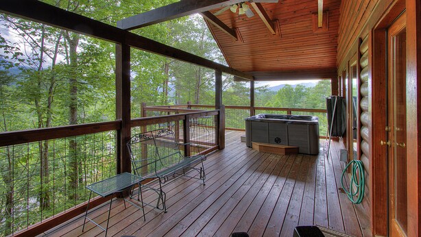 A wooden deck with a hot tub, a table, and chairs, overlooking a forested area. - Book NOW and receive tickets to Dollywood, Anakeesta and many more (Gatlinburg)