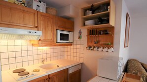 A compact kitchen with wooden cabinets, a microwave, a sink, and a small table with a kettle. - Cozy Ski-In/Ski-Out Apartment for 4 in Arêches-Beaufort, Terrace, Great Amenities (Arêches-Beaufort)