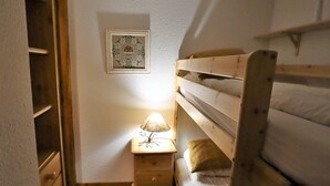 A small, cozy room with bunk beds, a wooden dresser, a nightstand with a lamp, and a framed picture on the wall. - Cozy Ski-In/Ski-Out Apartment for 4 in Arêches-Beaufort, Terrace, Great Amenities (Arêches-Beaufort)