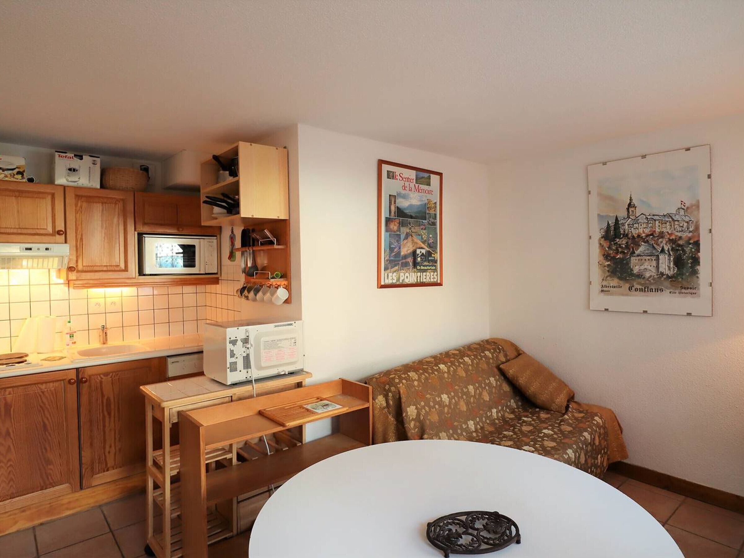 A compact kitchen with wooden cabinets, a microwave, and a small table with a kettle.