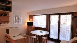 A compact kitchen with a microwave, a small dining table with four chairs, a television on a wooden cabinet, and a sliding glass door leading to a balcony. - Cozy Ski-In/Ski-Out Apartment for 4 in Arêches-Beaufort, Terrace, Great Amenities (Arêches-Beaufort)