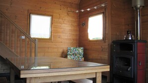 A wooden cabin interior with a staircase, a glass-top table, a colorful cushion, and a wood-burning stove. - Eco-friendly house in the French countryside (Donzy)