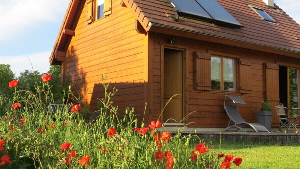 A wooden cabin with a sloped roof, solar panels, and a small porch with outdoor seating. - Eco-friendly house in the French countryside (Donzy)