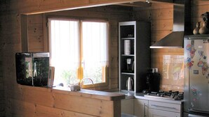 A kitchen with wooden walls, a built-in microwave, a refrigerator, and a window providing natural light. - Eco-friendly house in the French countryside (Donzy)