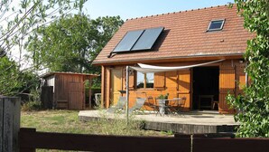 A wooden cabin with a tiled roof, a small porch with outdoor seating, and solar panels on the roof. - Eco-friendly house in the French countryside (Donzy)