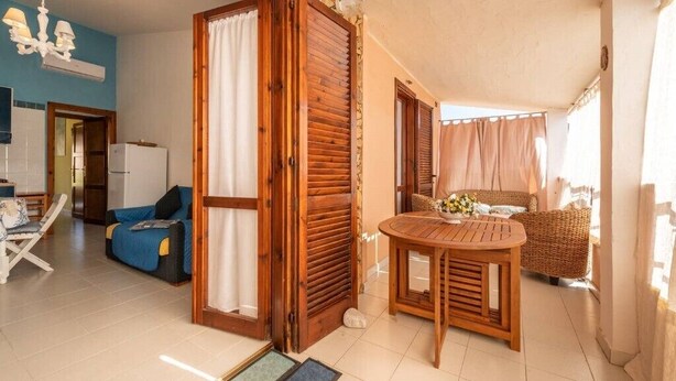 Um quarto acolhedor com porta de madeira, uma mesa de jantar, uma cadeira de vime e um sofá.