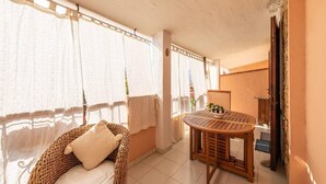 Um quarto aconchegante com uma cadeira de vime, uma mesa de madeira e vista através de cortinas leves.