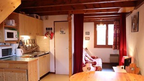 A cozy kitchen with wooden cabinets, a microwave, and a sink. There is a dining table with chairs and a red curtain in the background. - Cozy duplex 33m² in Arêches-Beaufort, 4 pers., ski-in/ski-out, pets allowed, parking (Arêches-Beaufort)