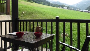 A wooden table with two red bowls and a pitcher on a balcony overlooking a green hillside with houses.