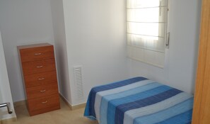 Cozy bedroom with a single bed, dresser, and window with blinds.