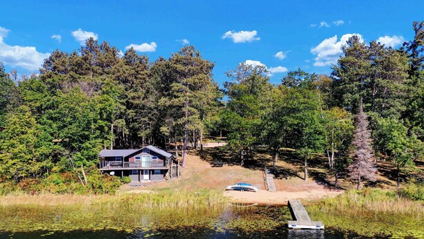 Una cabaña junto al lago con un muelle, rodeada de un bosque denso.